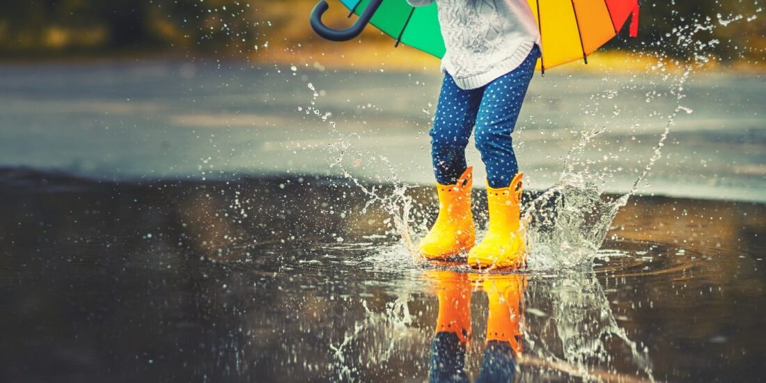 Child jumping into a puddle with yellow wellington boots on.
